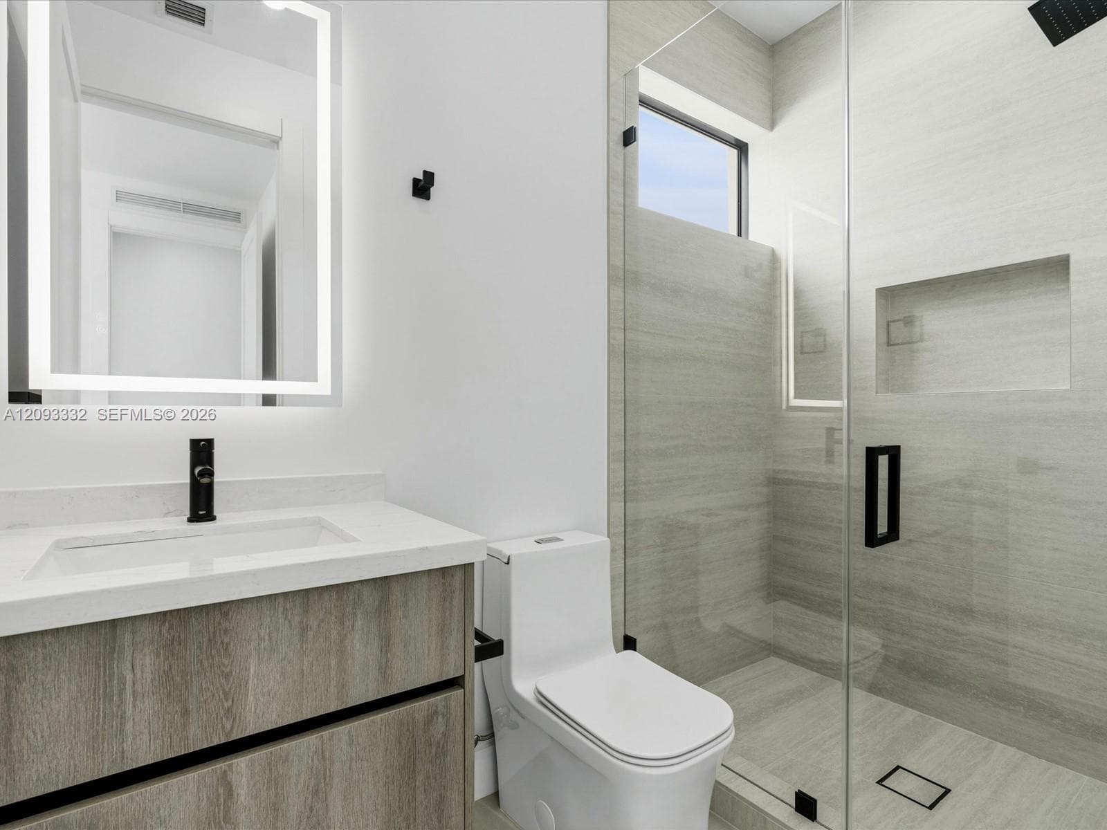 Floating vanity with a light wood-finish cabinetry, rectangular integrated sink, illuminated LED mirror, and matte black hardware
