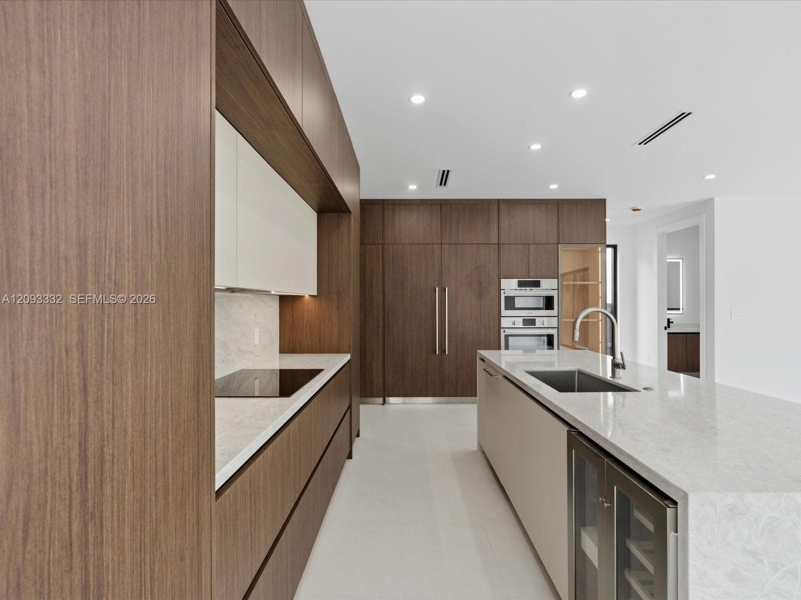 Modern kitchen featuring custom wood-finish cabinetry, stone-surface countertops, a large center island with integrated wine refrigeration, and stainless steel wall-mounted double ovens