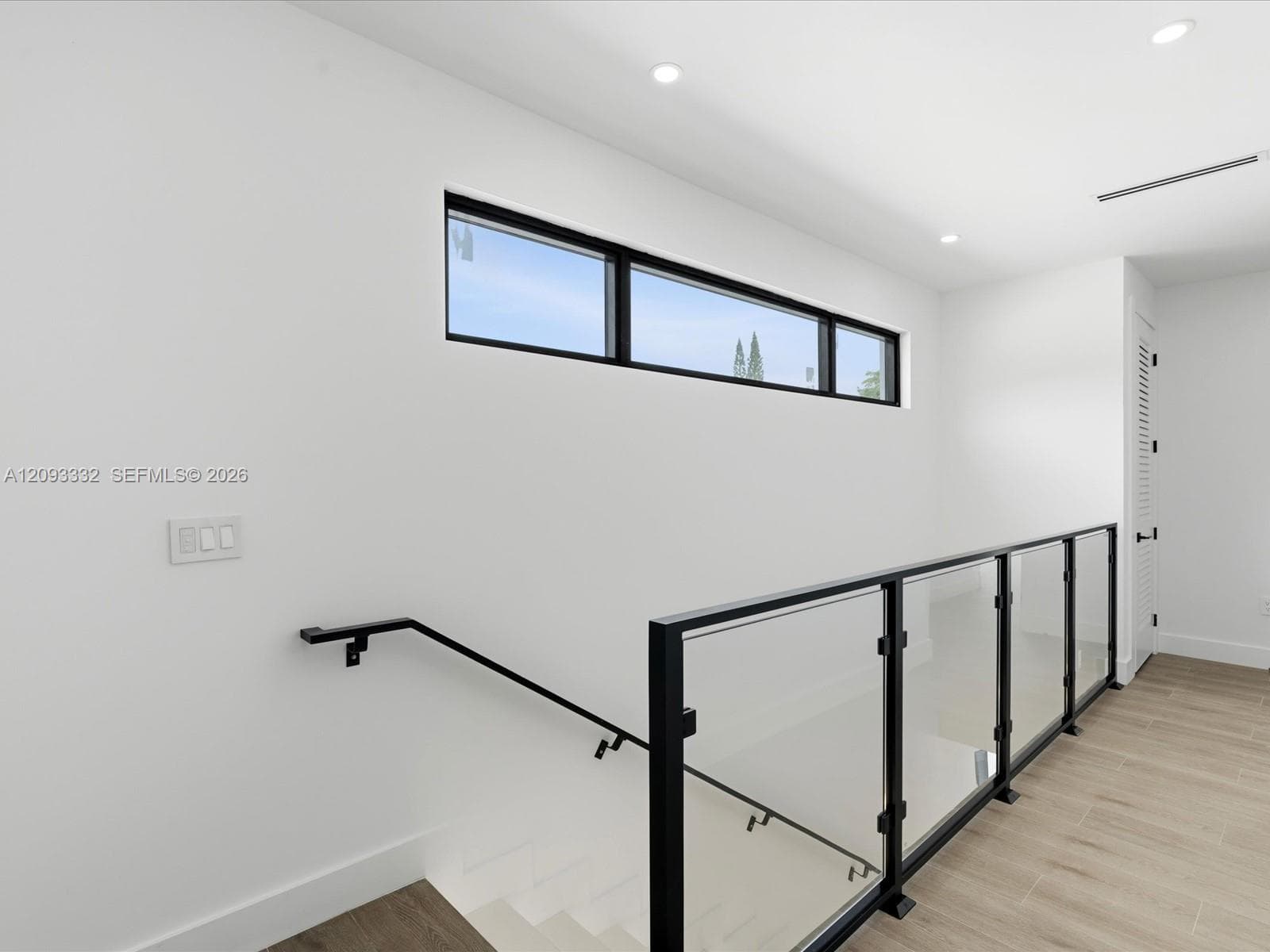 Modern staircase featuring a black metal railing with glass panels, wood-finish flooring, recessed lighting, and a horizontal clerestory window