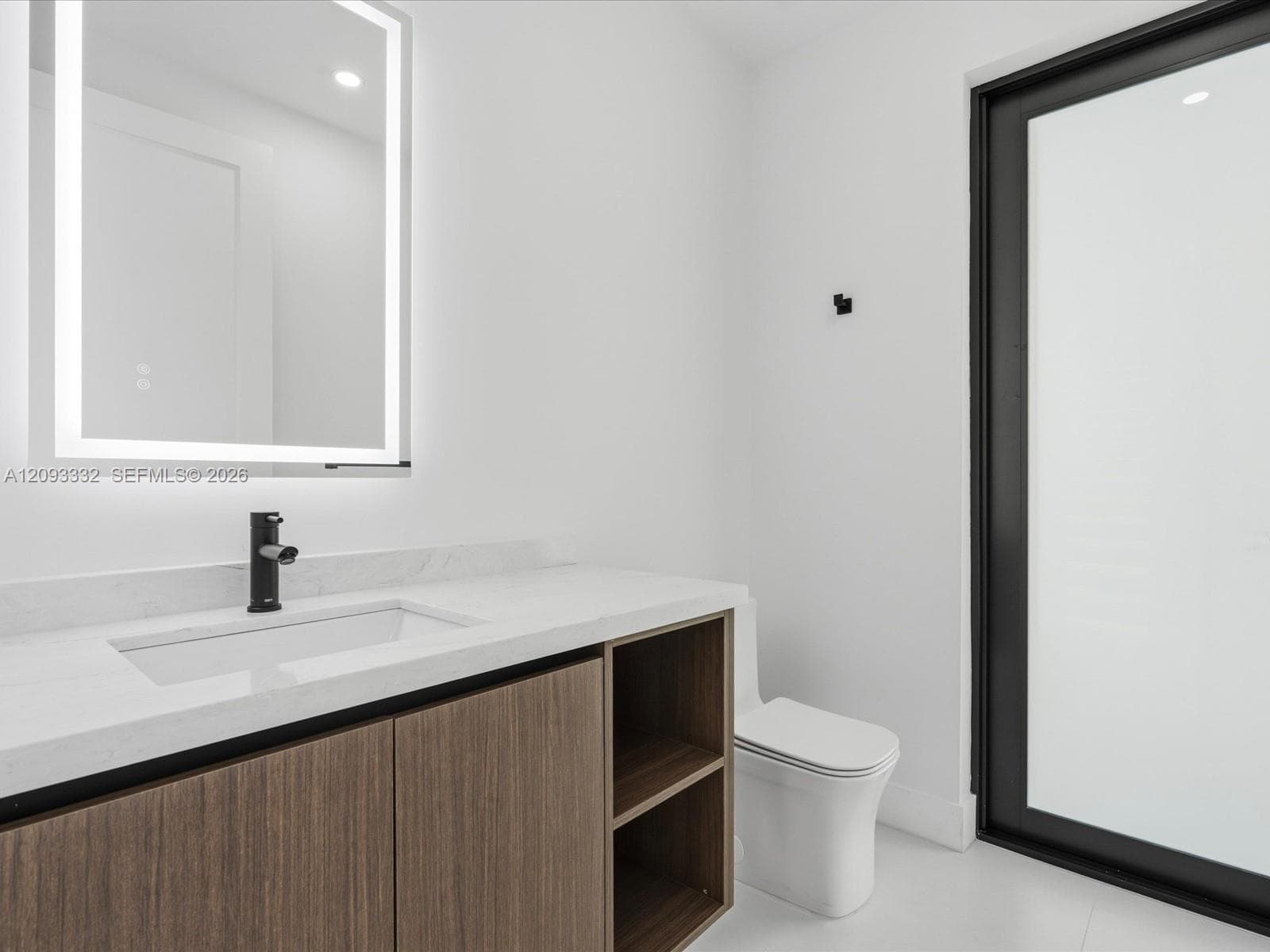Wood-finish floating vanity with white stone countertop, rectangular undermount sink, matte black faucet, integrated LED-backlit mirror, and matte black framed door with frosted glass