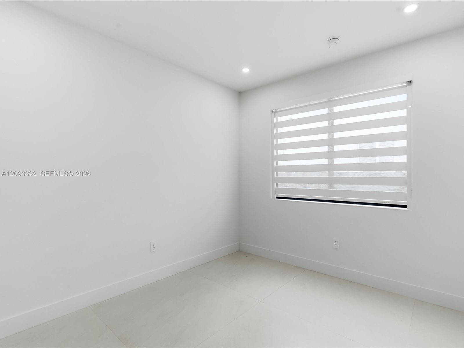 Neutral-toned interior space featuring large-format tile flooring, recessed lighting, and a window equipped with striped roller shades