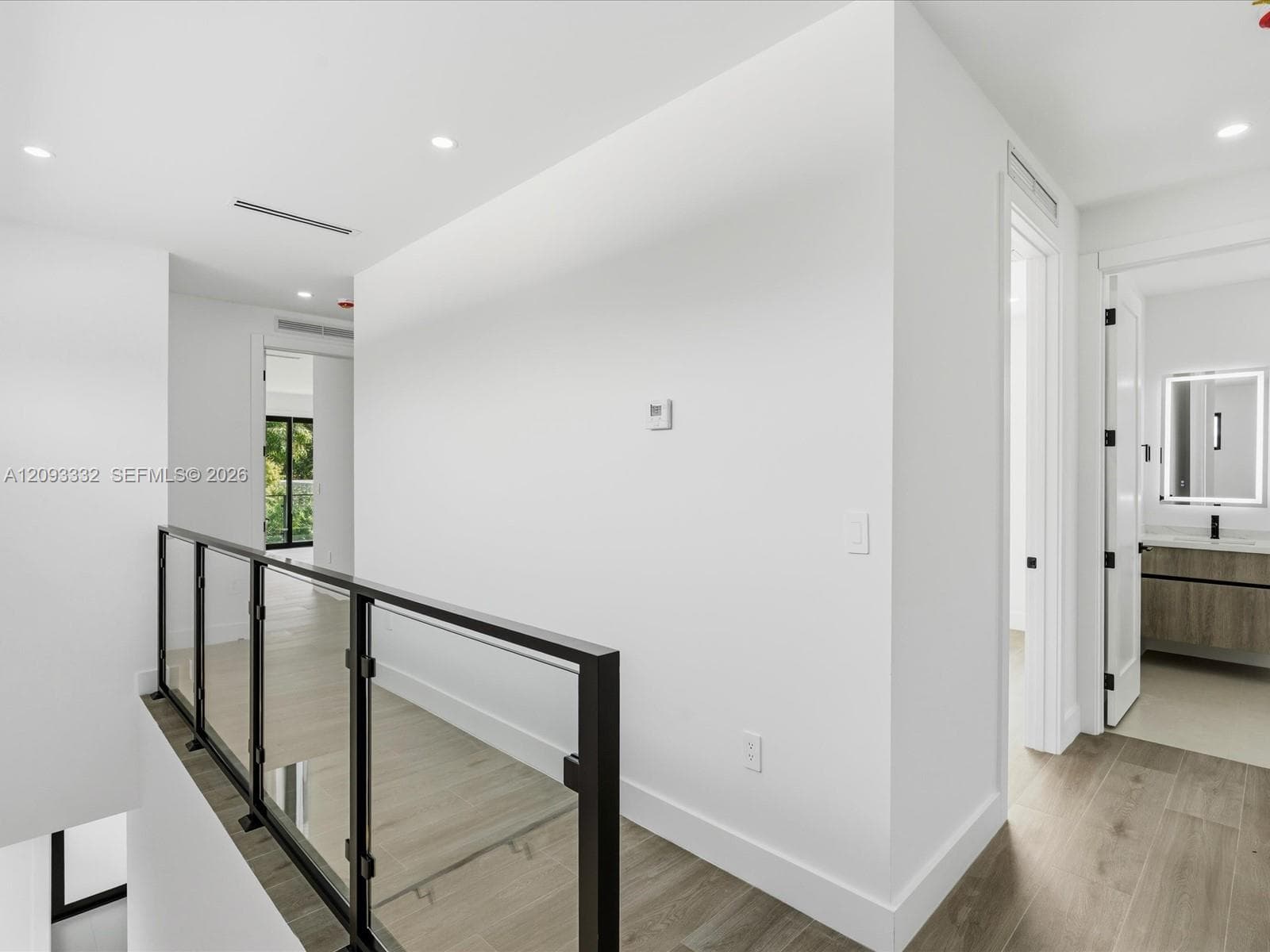 Hallway featuring wood-finish flooring, recessed lighting, and a metal railing with glass panel inserts