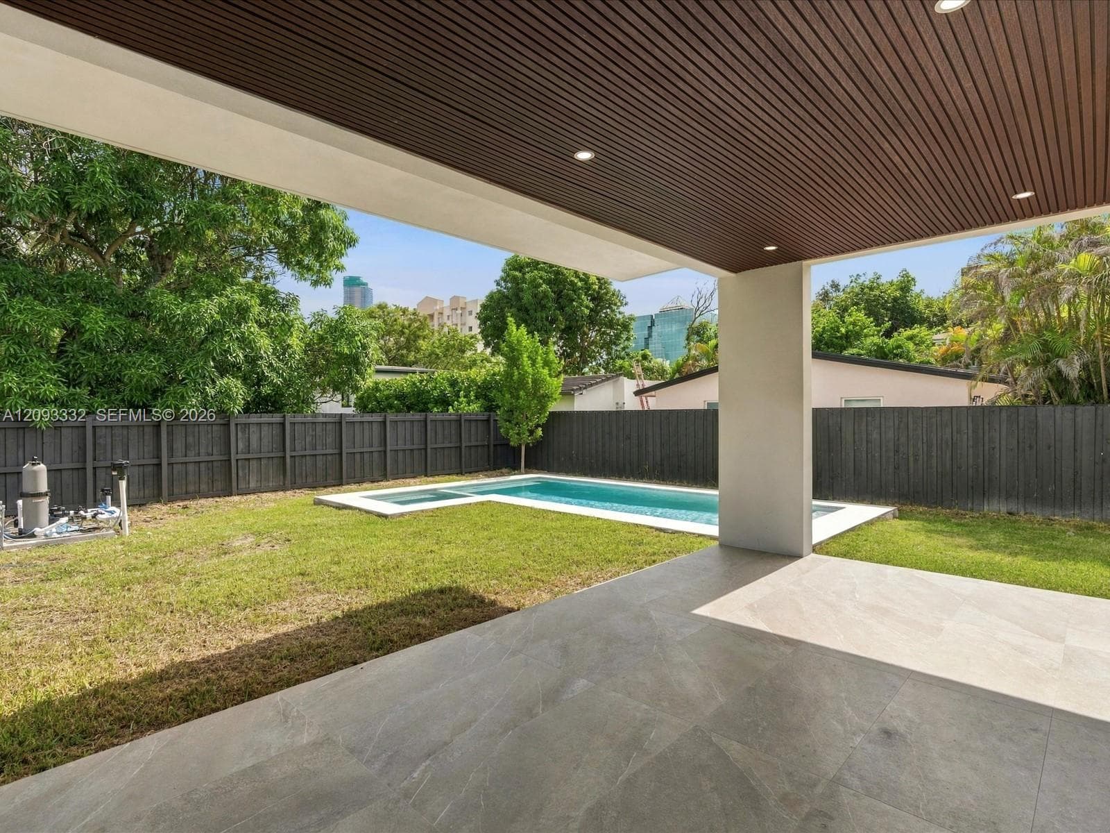 Covered outdoor patio featuring recessed lighting and wood-slat ceiling finish, complemented by a swimming pool with integrated spa and dark-tone privacy fencing