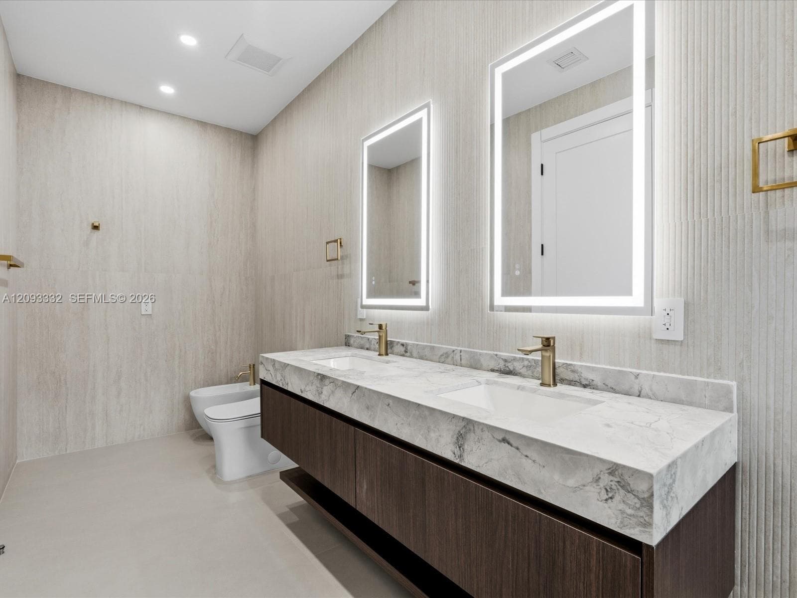 Floating dual-sink vanity featuring stone countertops, dark wood-finish cabinetry, integrated LED-backlit mirrors, and brass fixtures