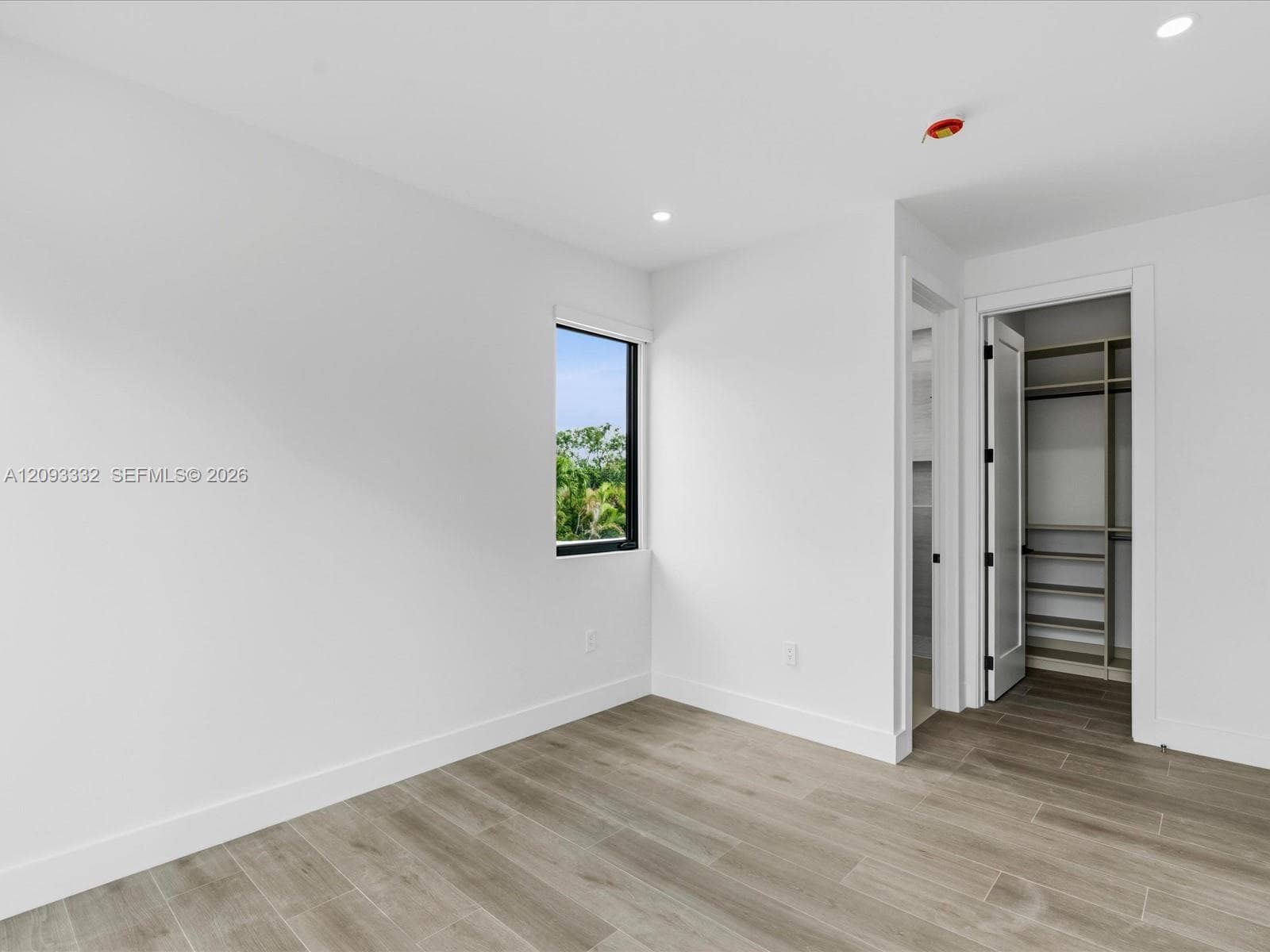 Neutral-toned interior featuring wood-finish flooring, recessed lighting, a single-pane black-trimmed window, and a walk-in closet with built-in shelving