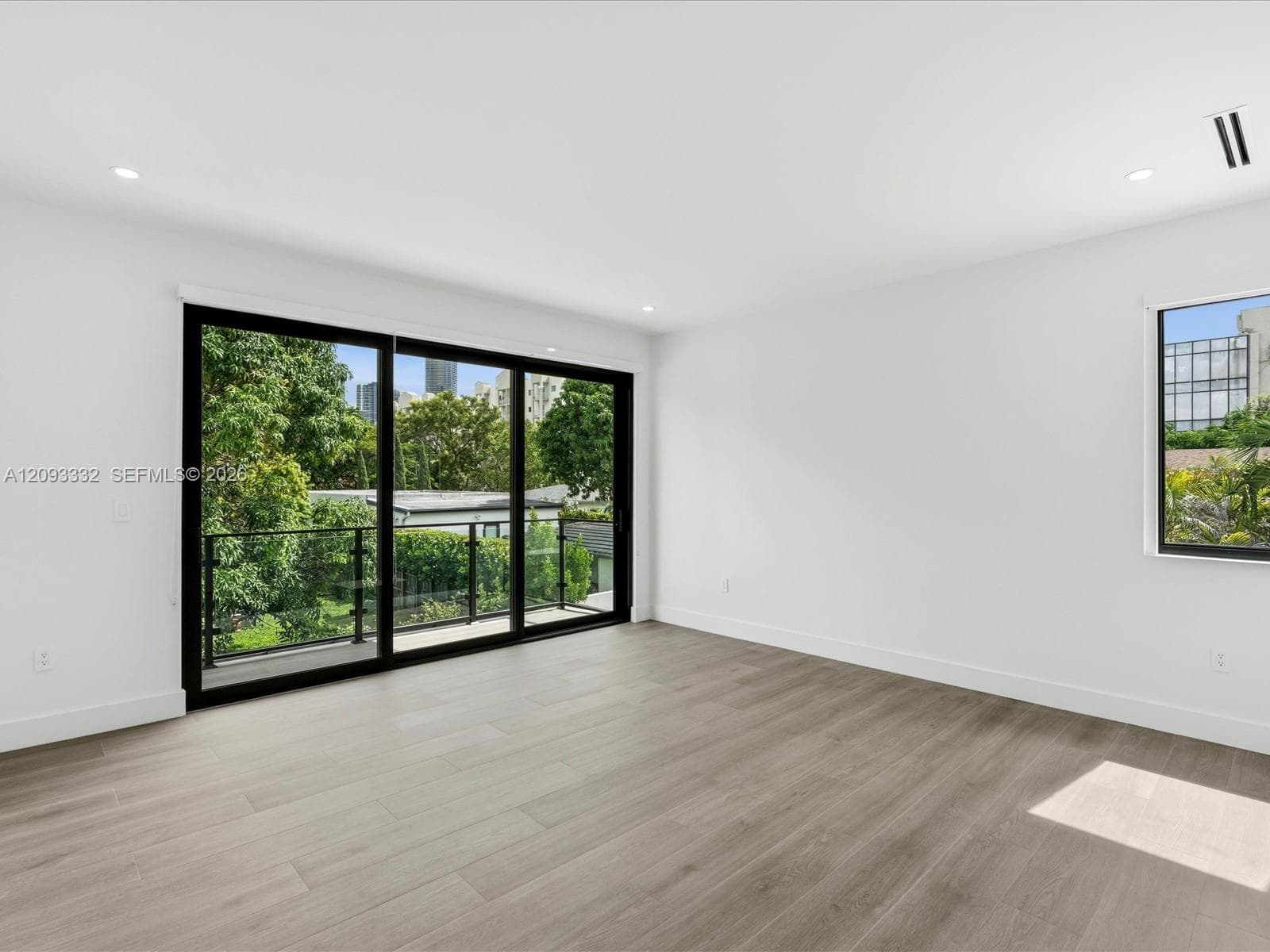 Interior space featuring wood-finish flooring, recessed lighting, and expansive floor-to-ceiling sliding glass doors opening to a balcony with a black metal railing