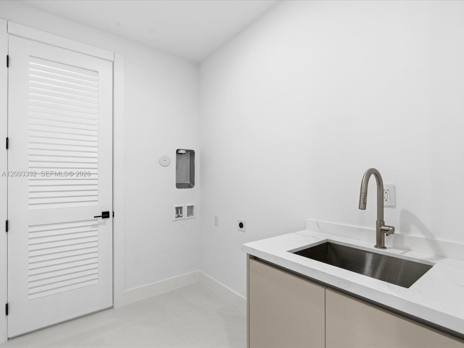 Utility area featuring a neutral-toned vanity with a stone-surface countertop, an integrated stainless steel drop-in sink, a high-arc faucet, and a white louvered door