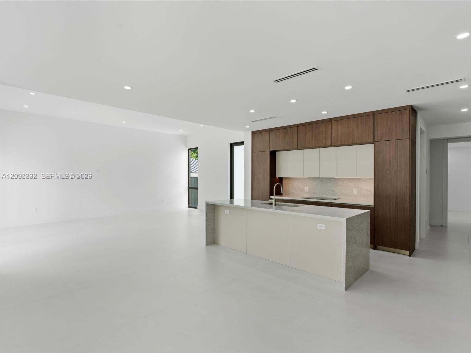 Modern kitchen featuring floor-to-ceiling cabinetry, a central island with stone-finish countertops, recessed lighting, and large-format tile flooring
