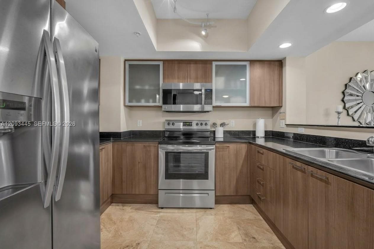 Kitchen cabinets modernized by A.I  Stainless steel appliances, wood-finish cabinetry, dark countertops, tile flooring, and recessed lighting-
