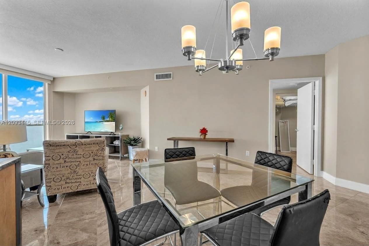 Expansive open-concept living area featuring a contemporary chandelier, large format tile flooring, and floor-to-ceiling windows