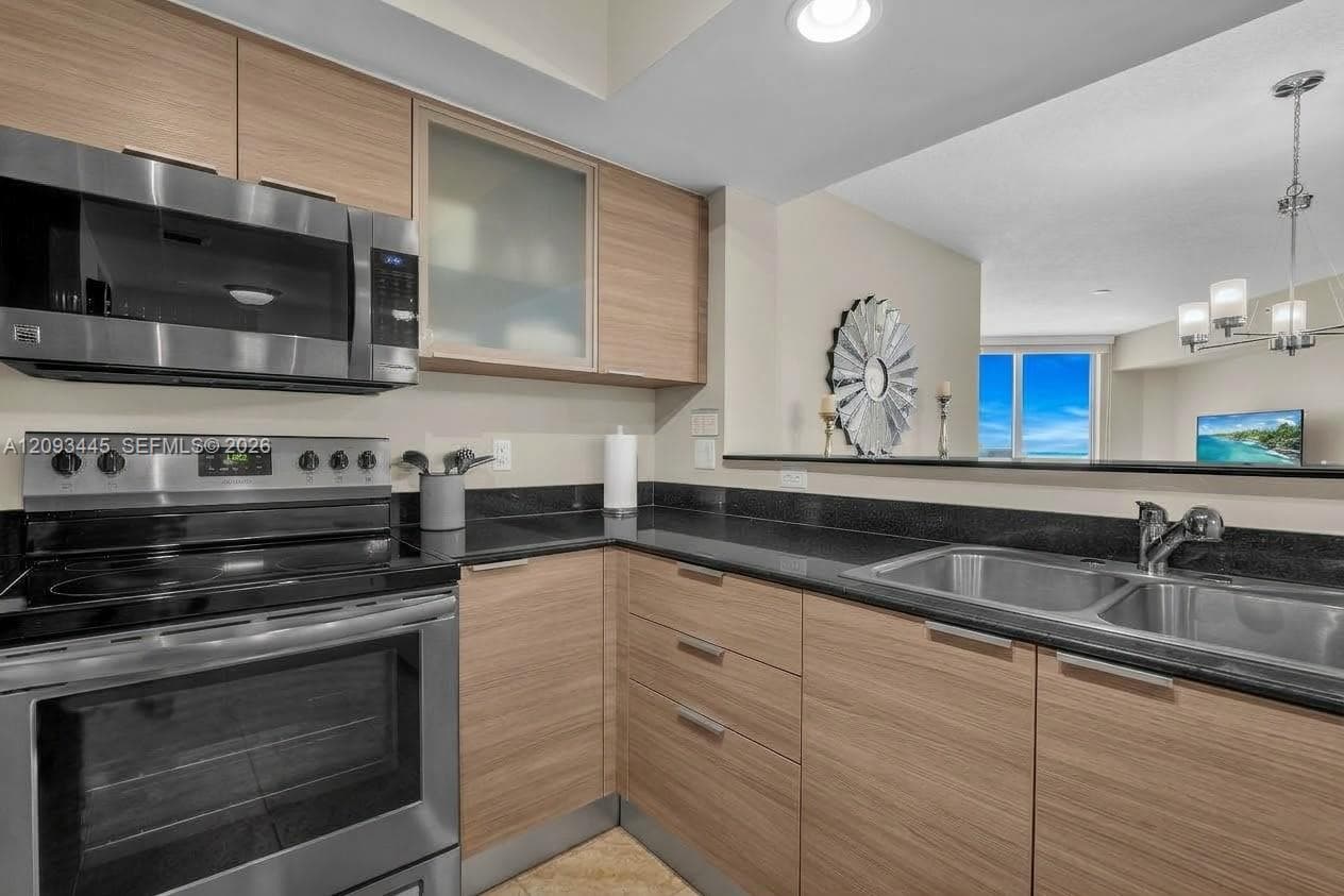 Kitchen cabinets modernized by A.I  Kitchen featuring dark wood-finish cabinetry, black countertops, stainless steel appliances, and recessed lighting