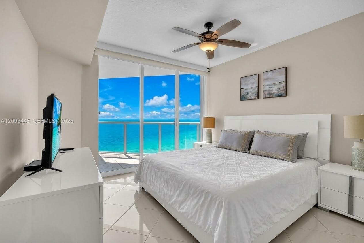 Floor-to-ceiling glass doors, private balcony, tile flooring, and a ceiling fan with integrated lighting