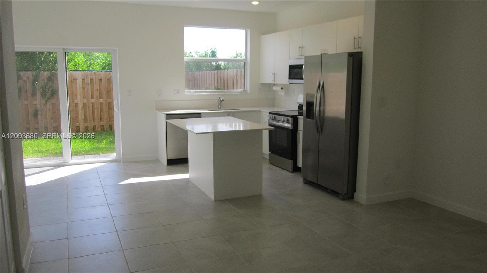 Kitchen featuring white cabinetry, an island with a quartz countertop, stainless steel appliances, tile flooring, and a sliding glass door