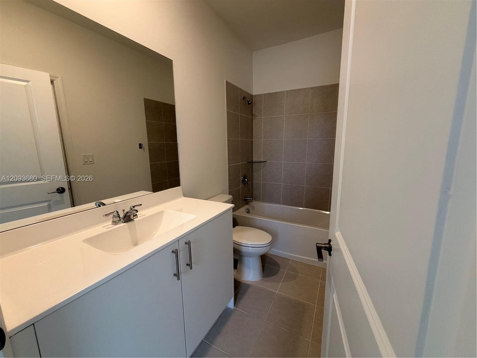 Bathroom featuring a white vanity cabinet with an integrated sink, large wall-mounted mirror, ceramic tile flooring, and a shower-tub combination with full-height neutral wall tile