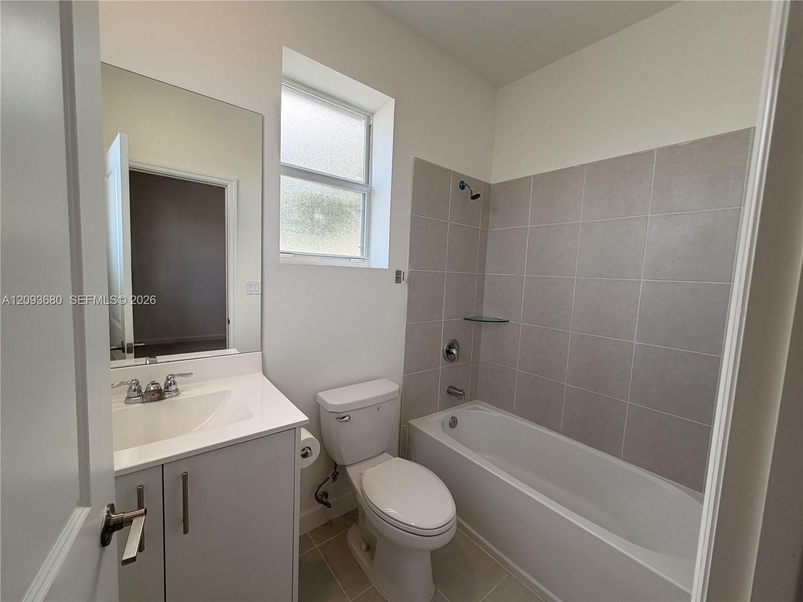 Full bathroom featuring a vanity with a white countertop, wall-mounted mirror, porcelain-finish tub with tiled surround, and frosted window