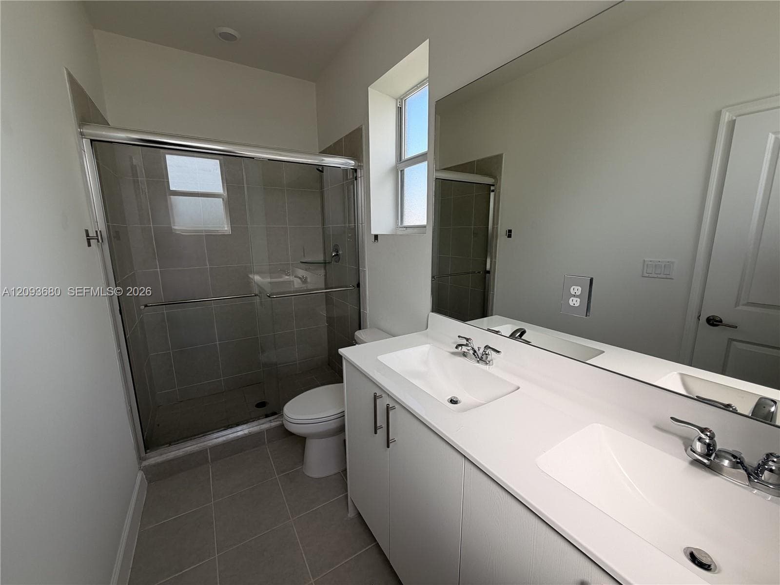 Double vanity with a composite countertop and integrated dual sinks, walk-in tiled shower with glass enclosure, and large-format tile flooring