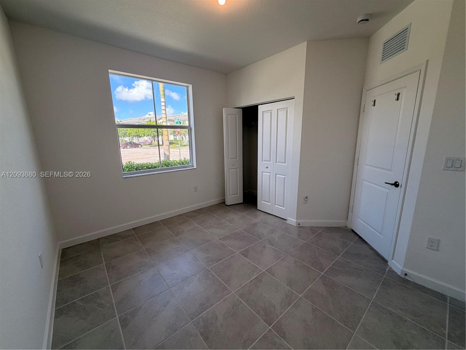 Room featuring large-format tile flooring, single-pane window, bi-fold closet doors, and a paneled interior door