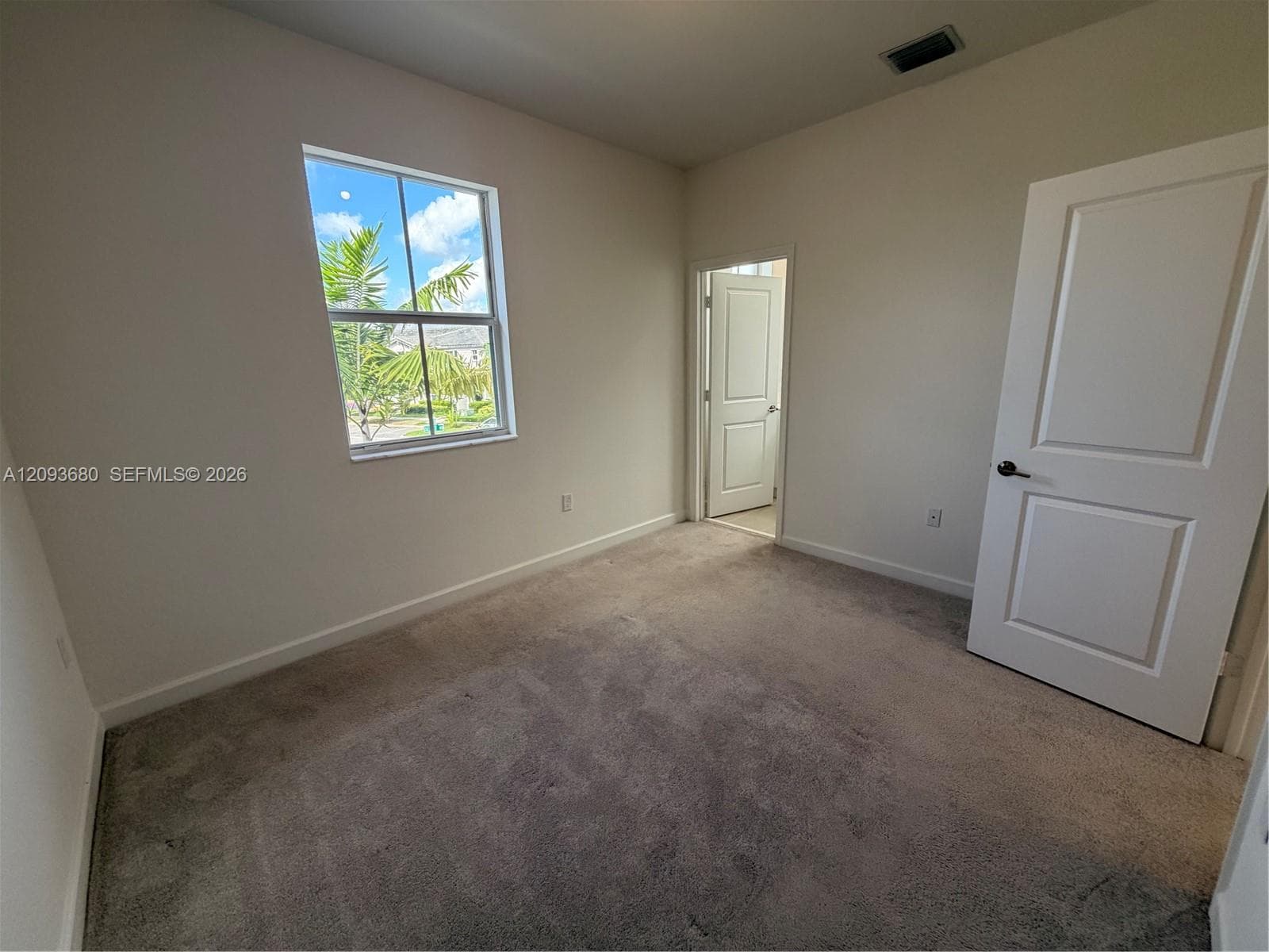 Neutral-toned interior space featuring neutral wall-to-wall carpeting, single-pane window with muntin detailing, and two solid-core interior doors with matte black hardware