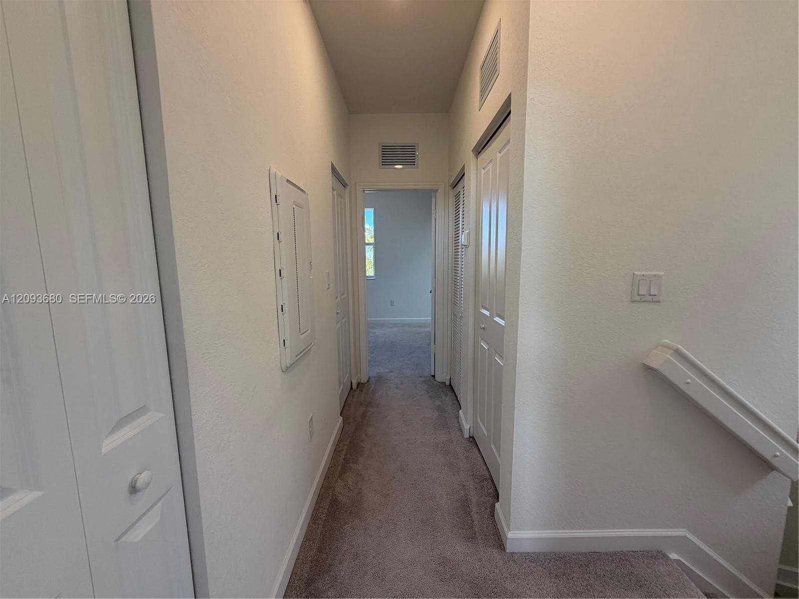 Interior hallway featuring wall-to-wall carpeting, paneled closet doors, and a painted wooden handrail