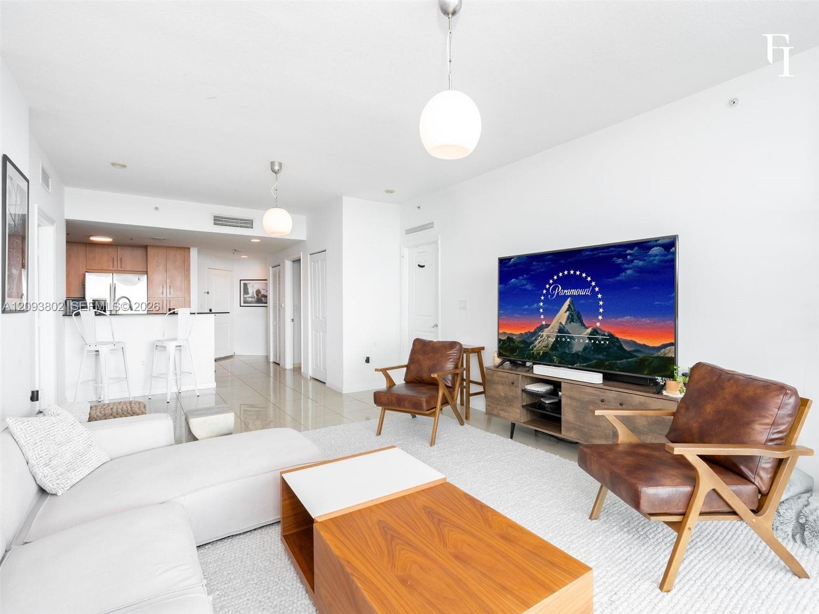Open-concept living space featuring high-gloss tile flooring, globe pendant lighting, and a kitchen peninsula with integrated seating