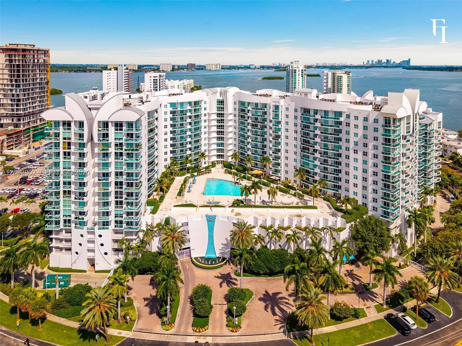 High-rise residential complex featuring a central outdoor swimming pool, integrated multi-level balconies, expansive water frontage, and professional landscaping with mature palm trees
