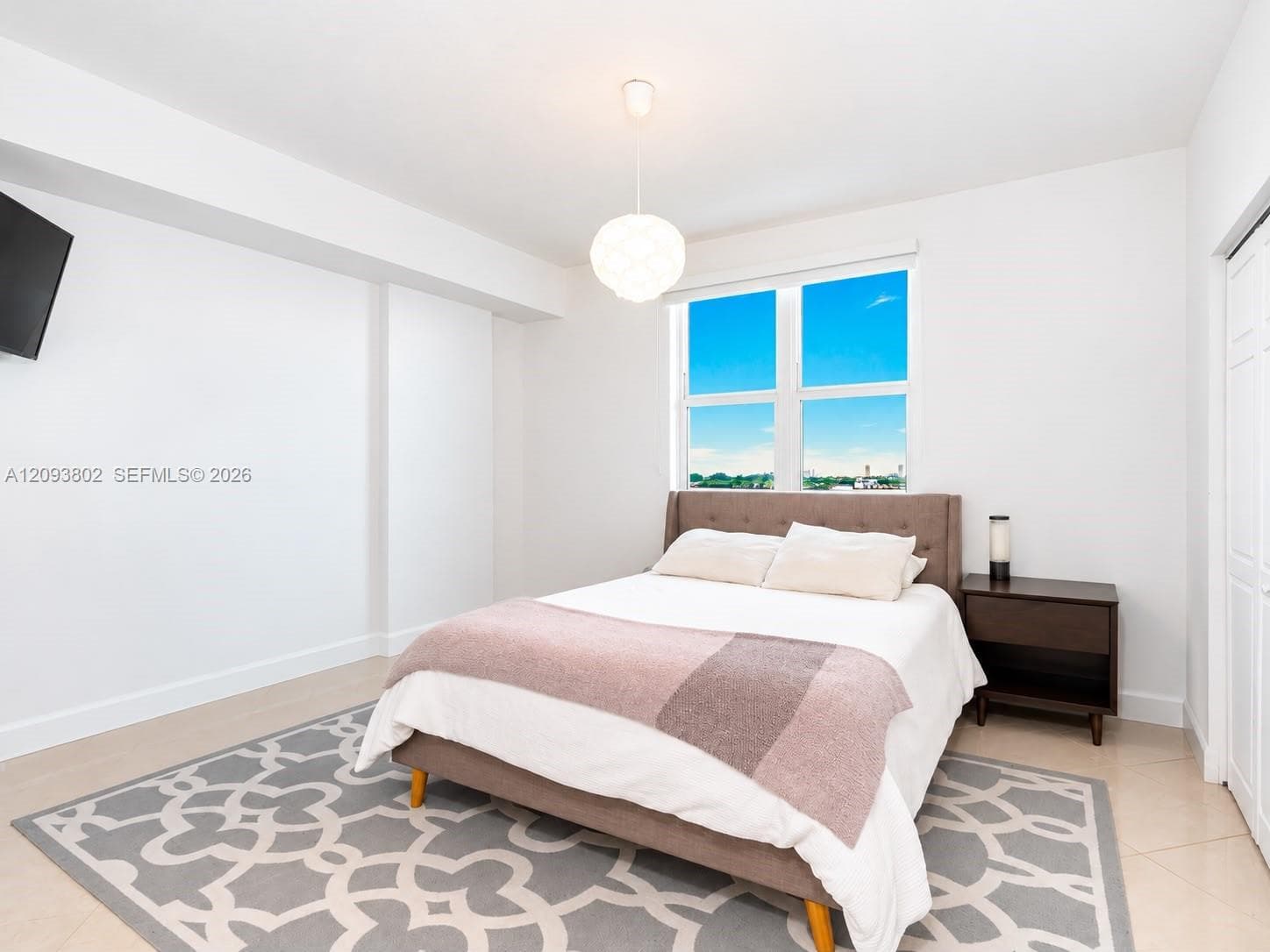 Neutral-toned interior space featuring light-colored tile flooring, bright white walls, large multi-pane window, and a modern globe pendant light fixture