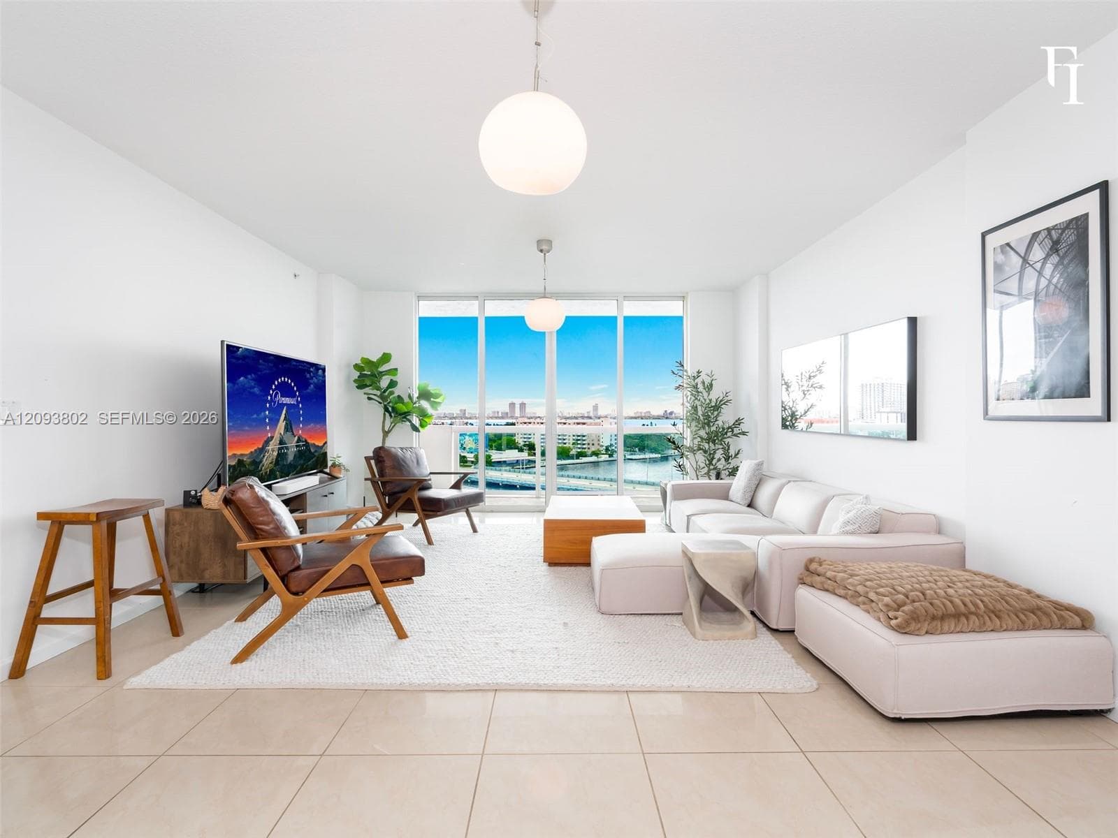 Open-concept living space featuring floor-to-ceiling glass windows, neutral tile flooring, and dual modern globe pendant light fixtures