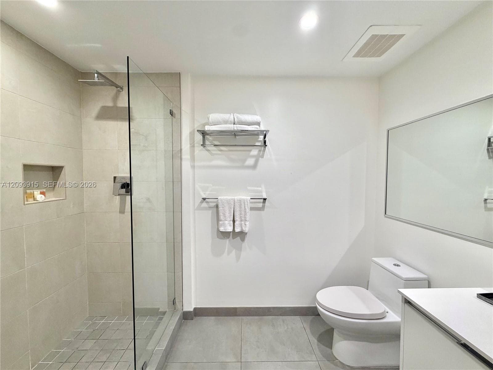 Walk-in shower featuring a frameless glass enclosure, rain-style shower head, and recessed wall niche, paired with a white vanity and large wall-mounted mirror