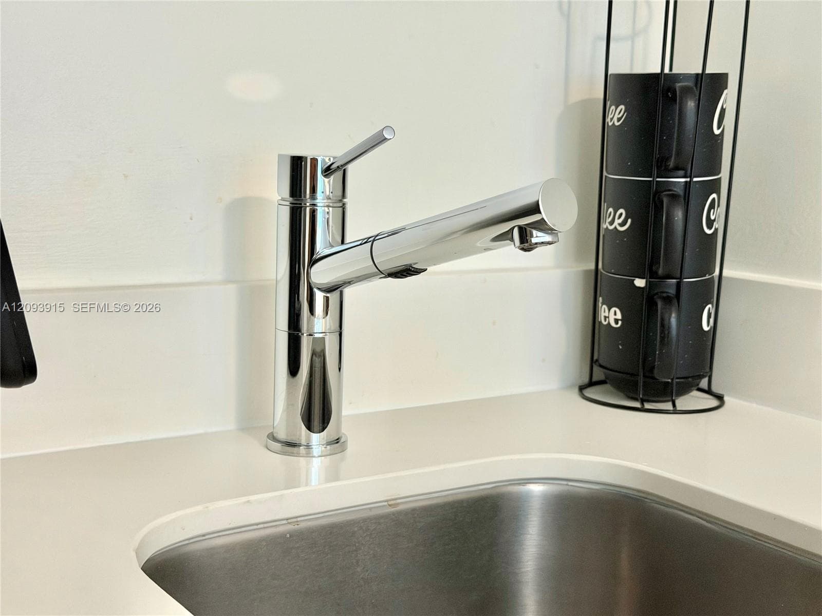 Chrome pull-down faucet with a single-handle lever, inset stainless steel sink, and solid-surface countertop with an integrated backsplash