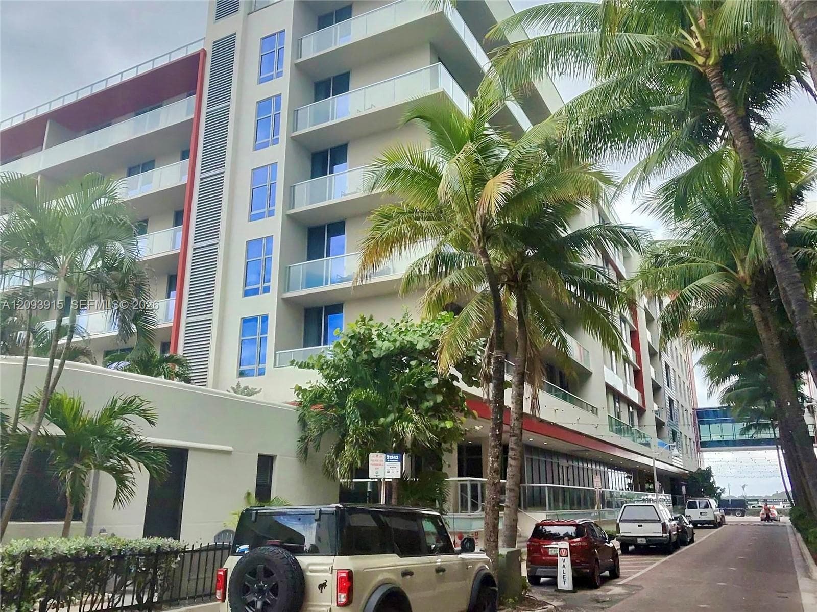 Mid-rise multi-story building featuring glass balcony railings, floor-to-ceiling windows, and red architectural accents