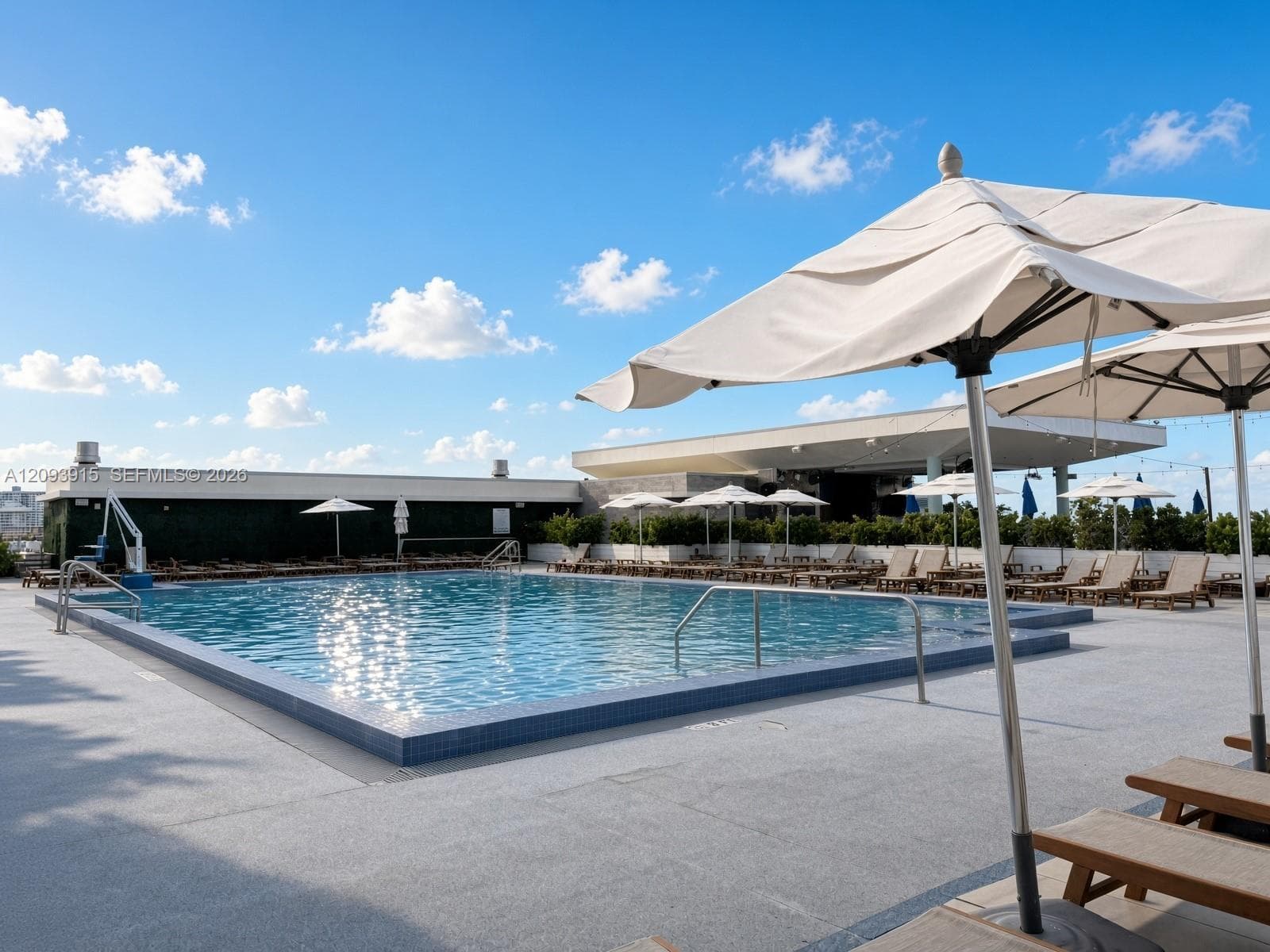 Rooftop swimming pool featuring a tiled waterline, metal handrails, a poolside lift, and a covered pavilion