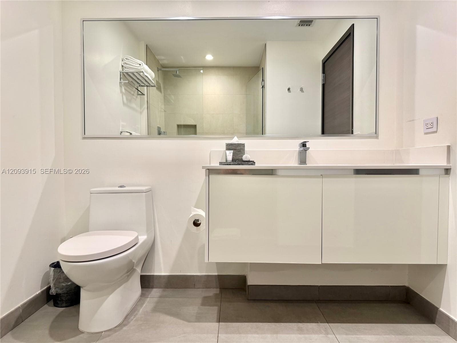 Wall-mounted floating vanity with integrated countertop, large-format mirror, contemporary single-handle faucet, and walk-in shower with glass enclosure