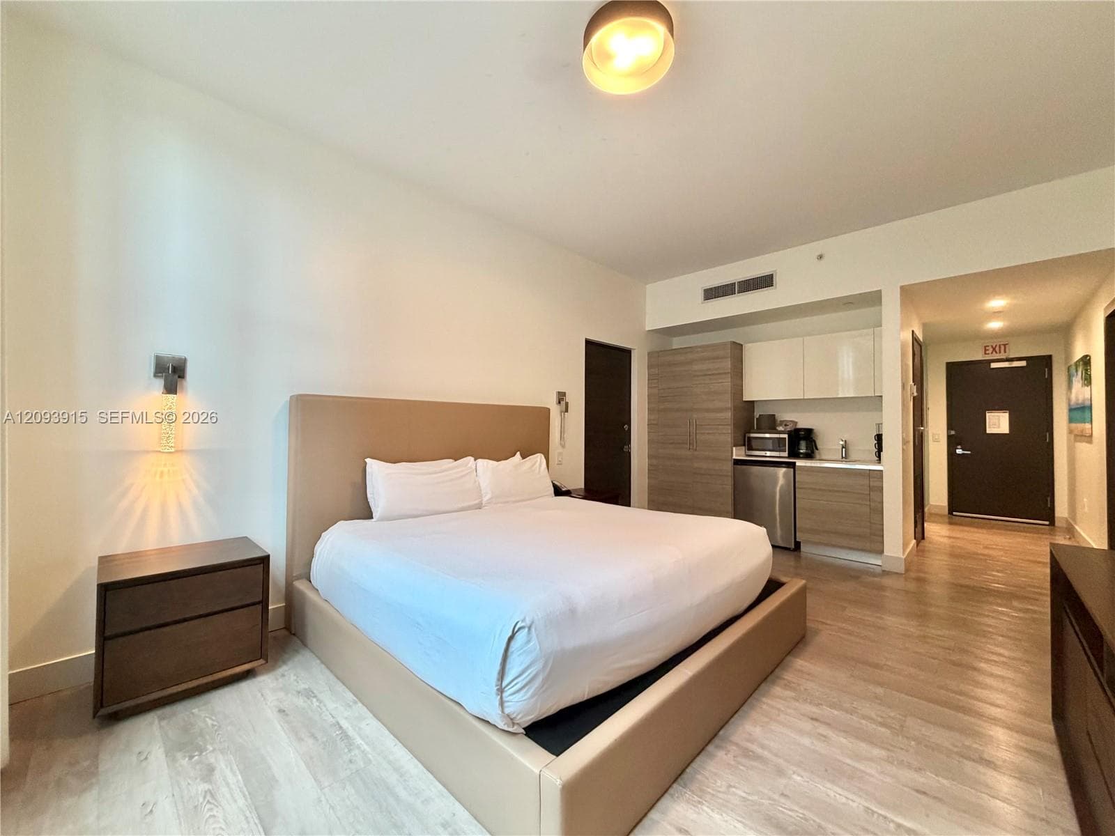Wood-finish flooring, kitchenette featuring light and wood-tone cabinetry, stainless steel mini-refrigerator, wall-mounted light fixture, and neutral wall palette