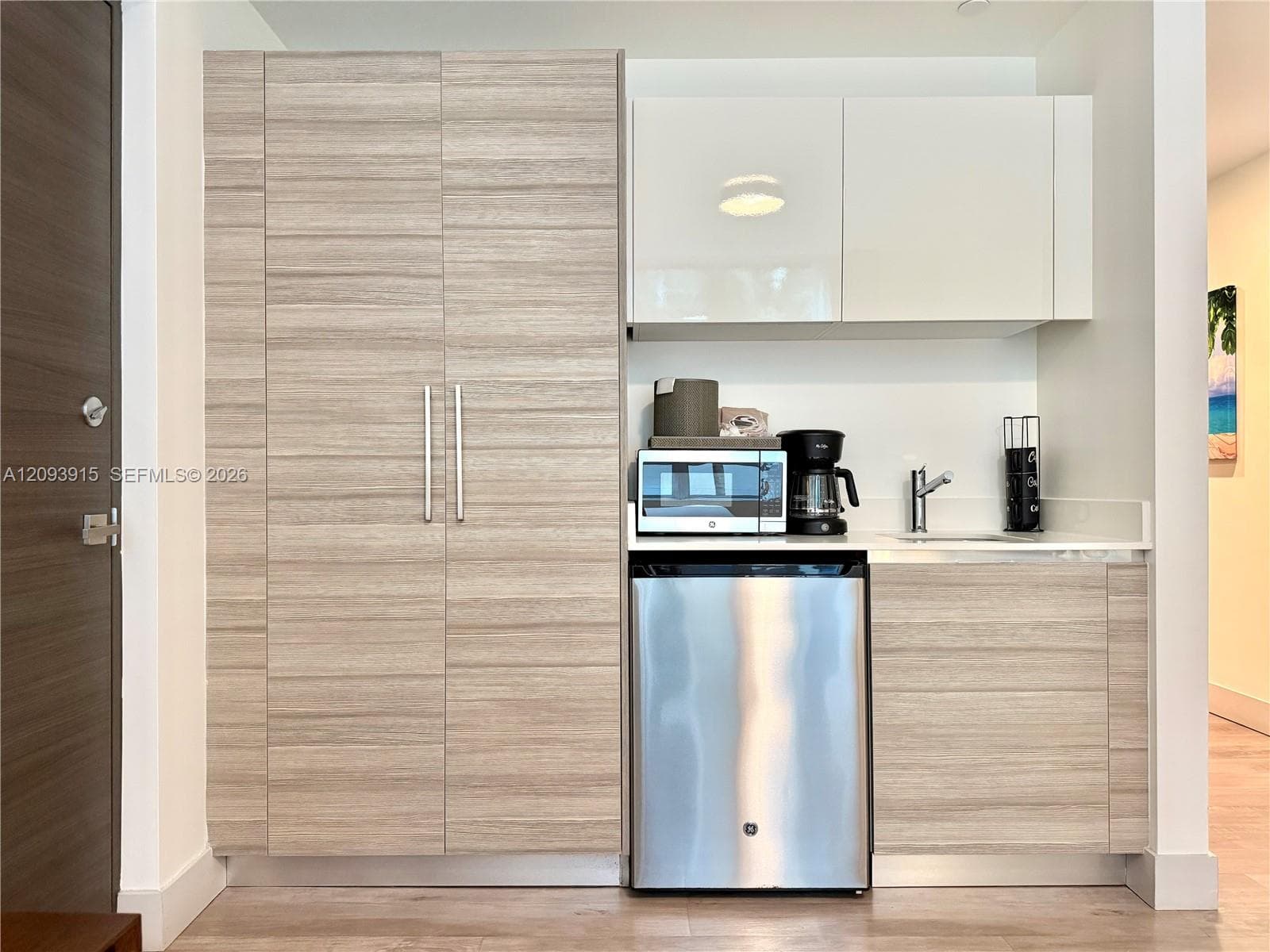 Built-in kitchenette featuring flat-panel wood-finish cabinetry, high-gloss upper cabinets, solid surface countertop, stainless steel mini-refrigerator, and undermount sink with a gooseneck faucet