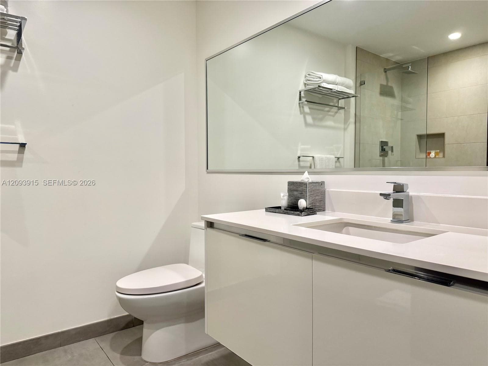 Modern floating vanity with a solid-surface countertop and integrated sink, large wall-to-wall mirror, and a glass-enclosed shower featuring a tiled niche