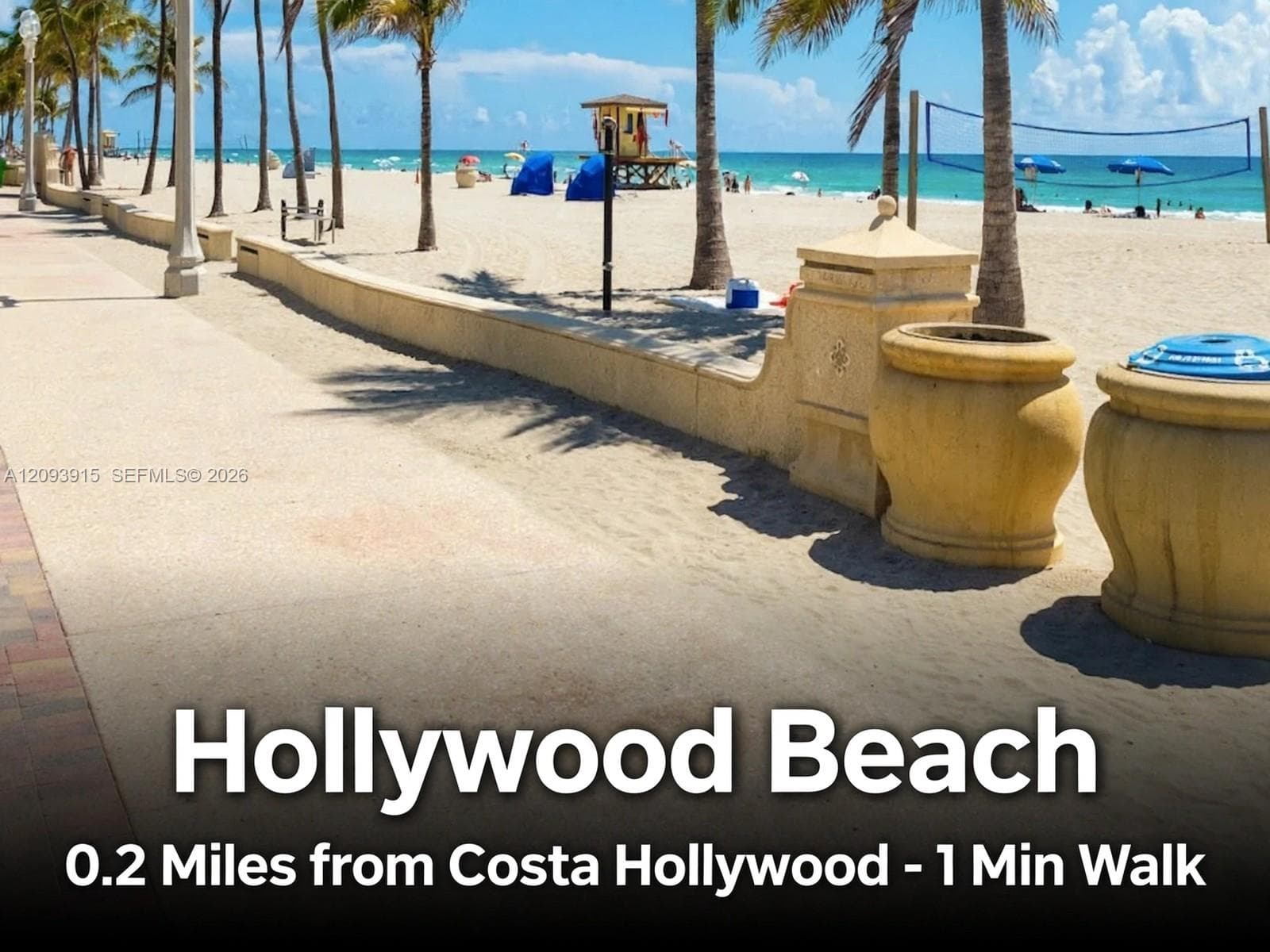 Paved concrete boardwalk featuring a masonry retaining wall, decorative stone planters, palm-lined landscape, and direct access to the sand beach