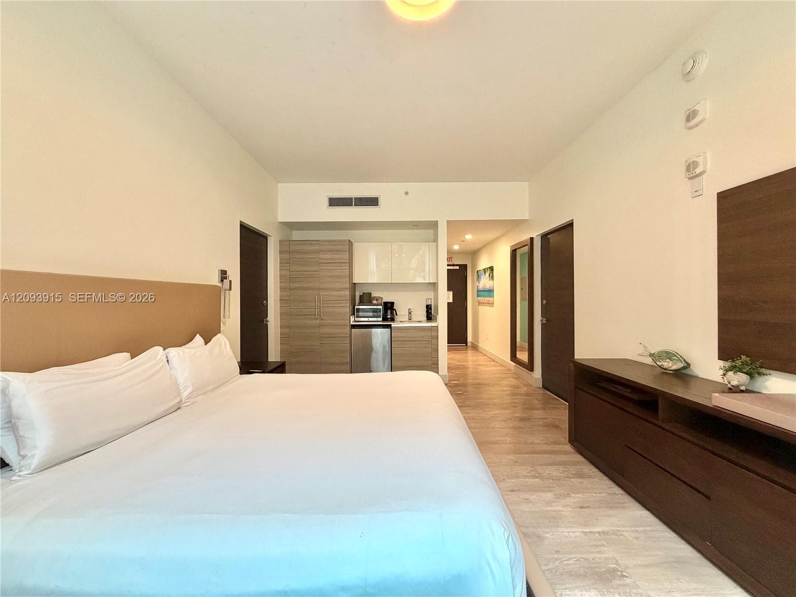 Efficiency suite featuring wood-finish flooring, a kitchenette with neutral-toned cabinetry, and a large built-in dresser