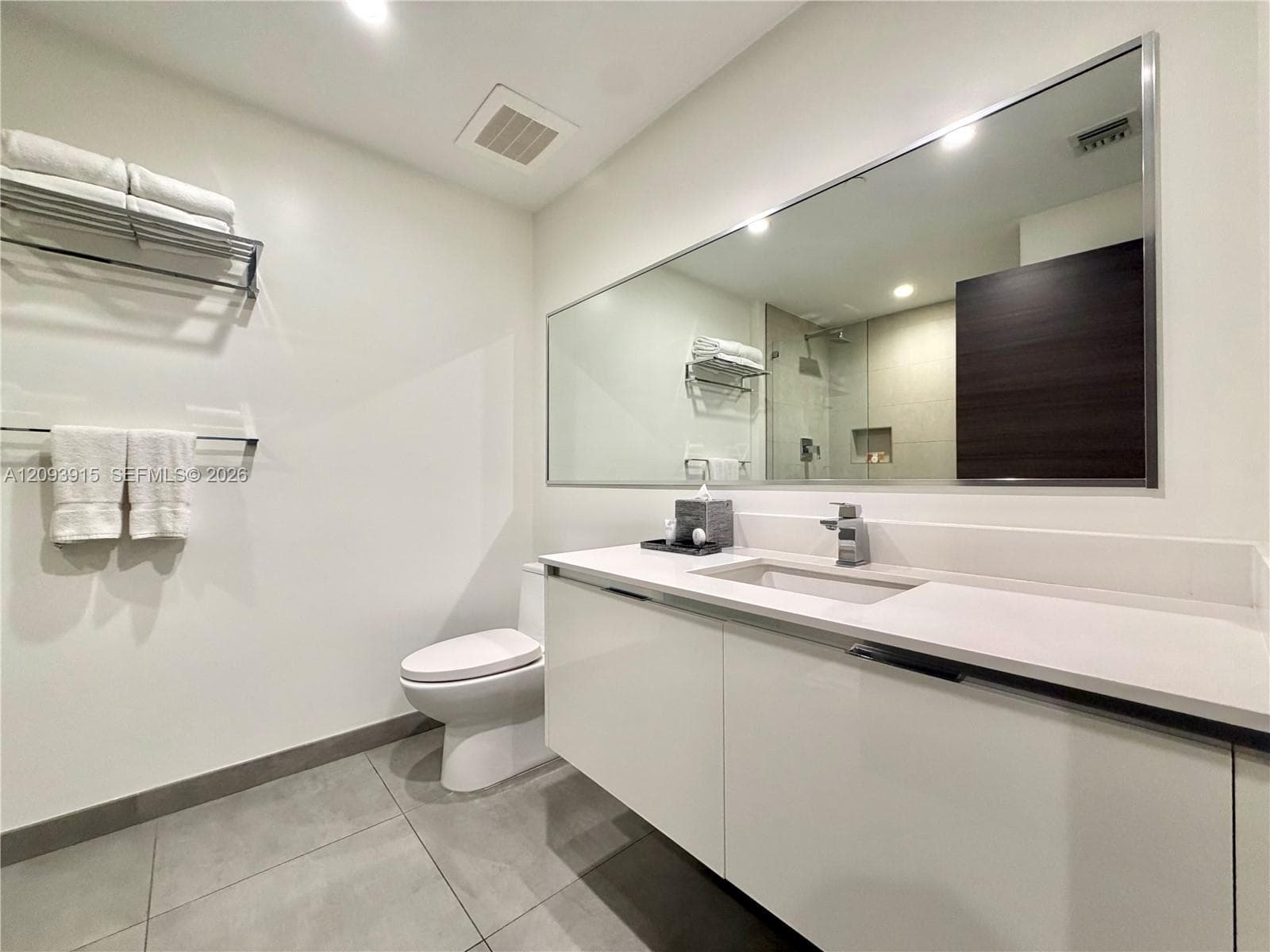Floating white vanity with solid-surface countertop and integrated sink, large wall-mounted mirror, matte metal faucet, and grey large-format floor tile