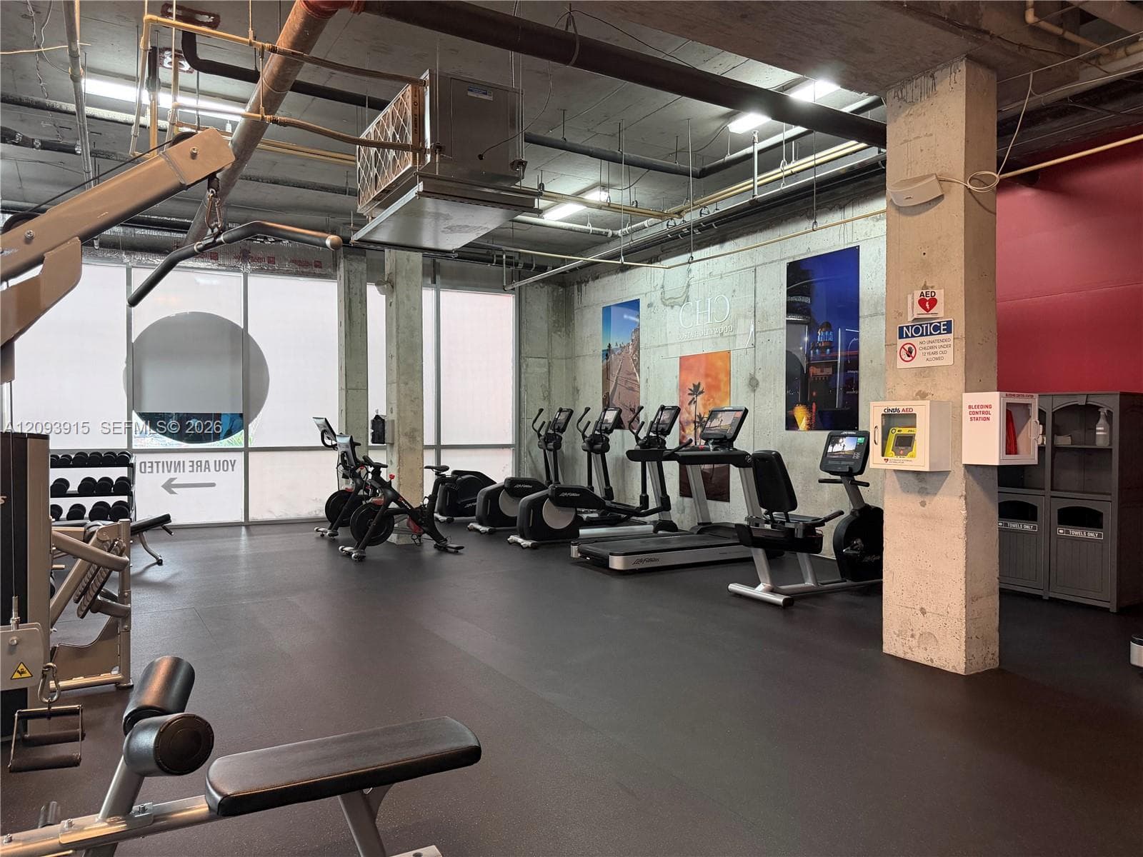 Fitness facility featuring rubberized flooring, exposed concrete structural elements, floor-to-ceiling windows, and integrated HVAC systems