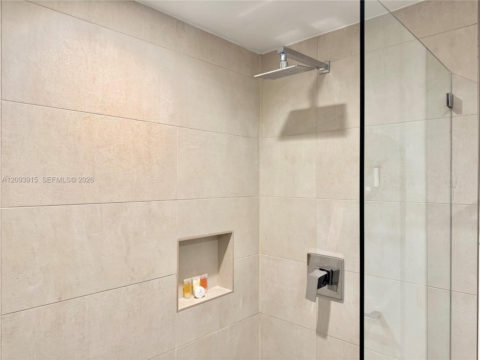 Shower enclosure featuring large-format neutral-toned wall tile, a built-in recessed wall niche, a square rainfall showerhead, and a frameless glass door