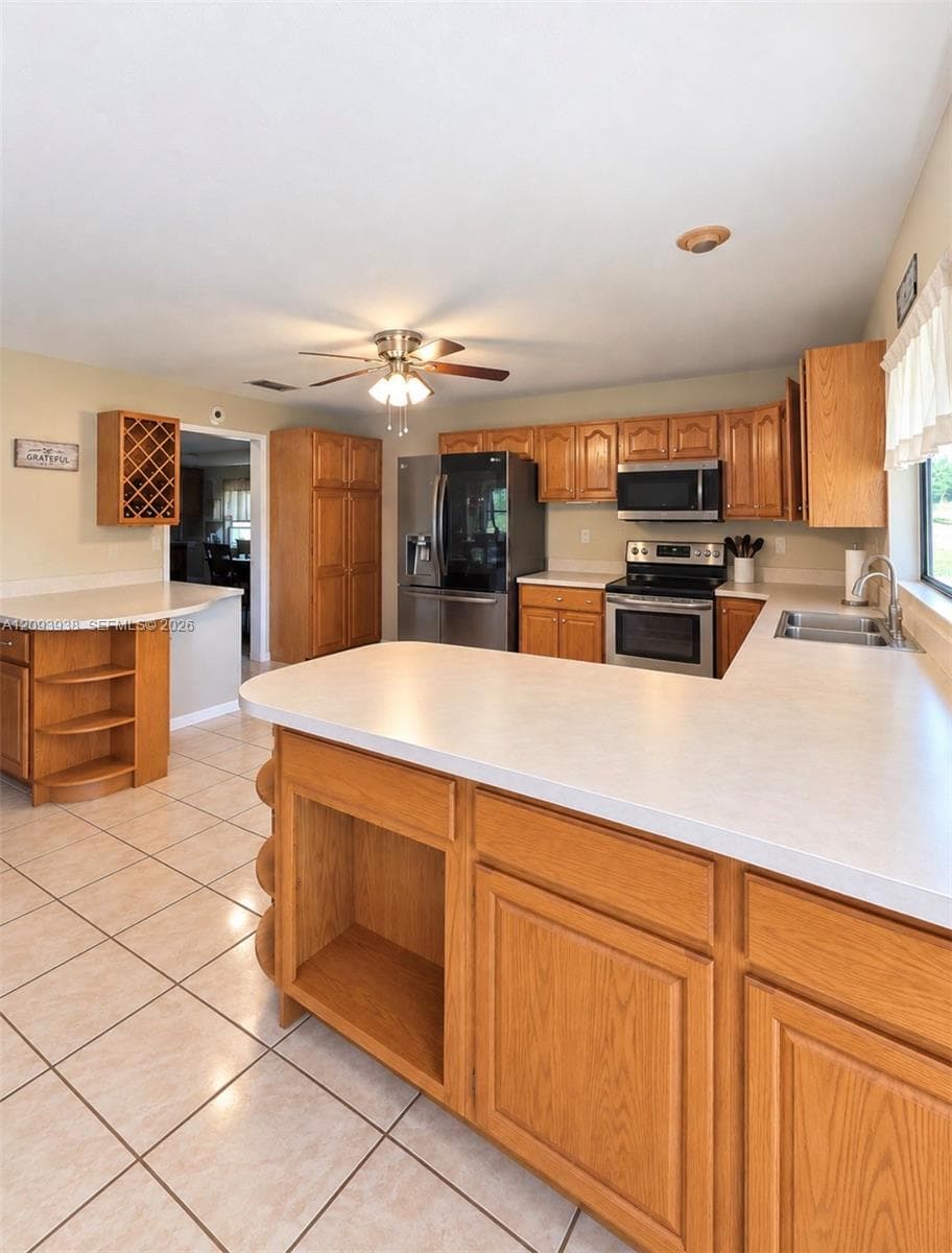 Kitchen featuring light wood cabinetry, integrated wine rack, solid-surface countertops, tile flooring, and stainless steel appliances