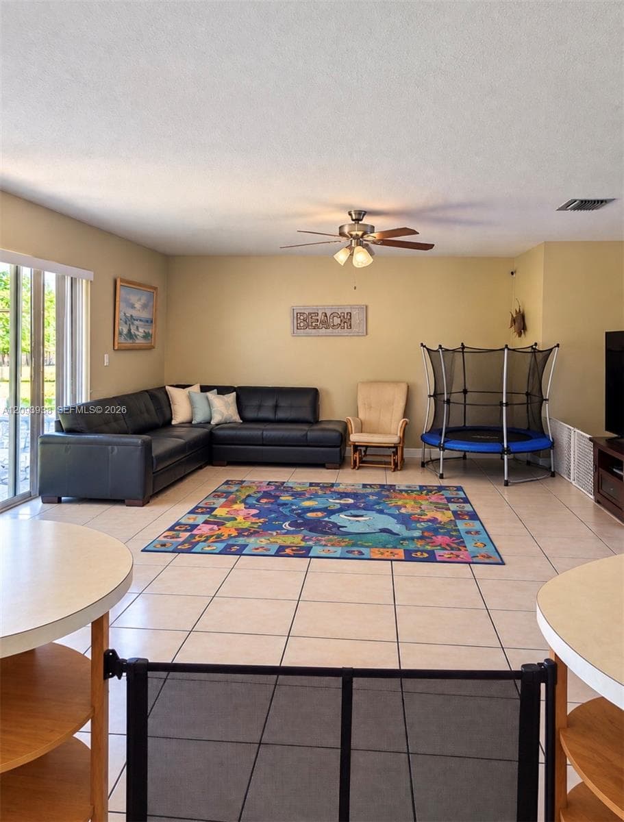 Spacious interior featuring large-format tile flooring, a multi-blade ceiling fan with integrated lighting, and expansive sliding glass doors