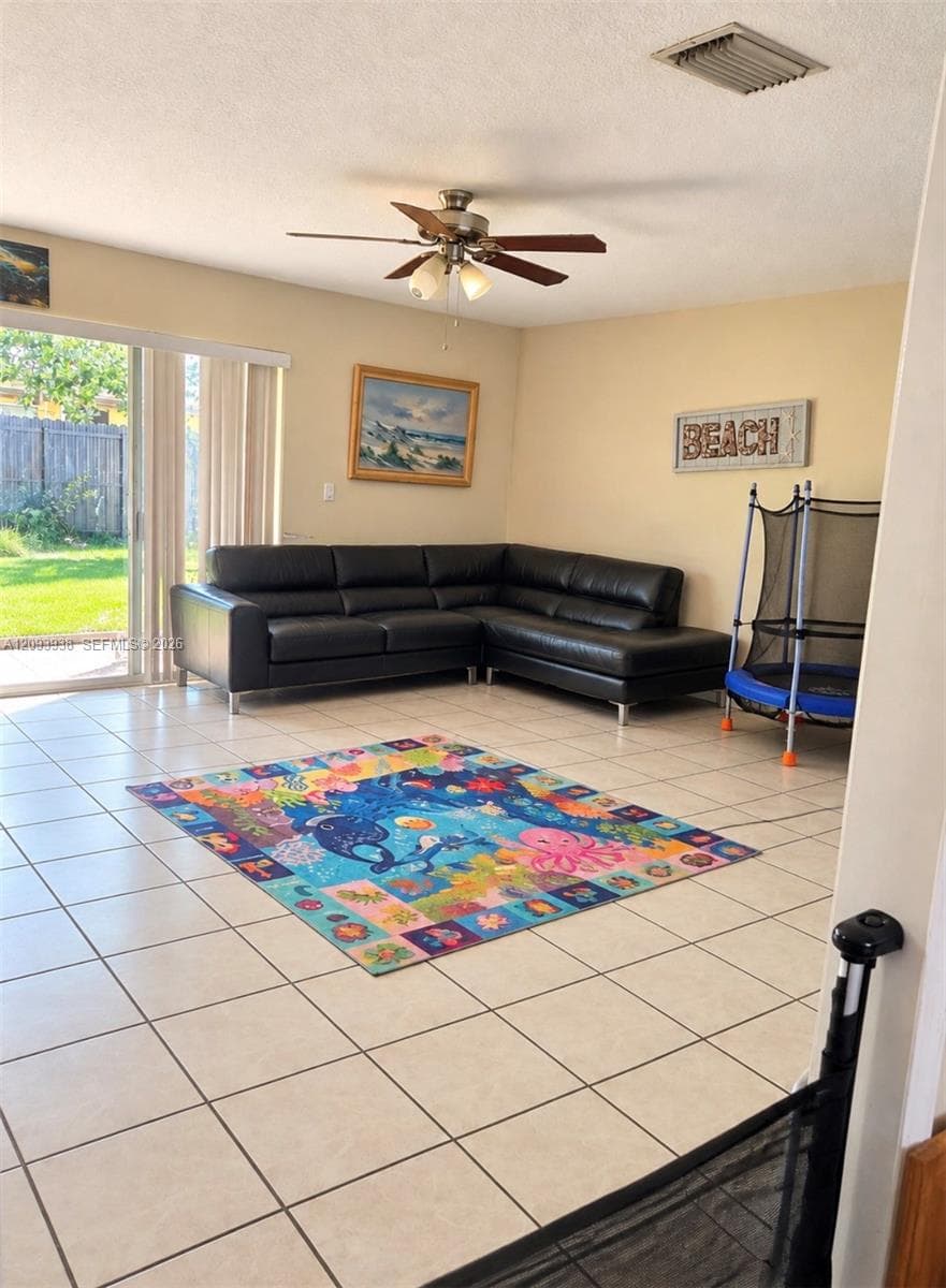 Open-concept living space featuring large-format tile flooring, a mounted ceiling fan with integrated lighting, and a sliding glass door providing exterior access