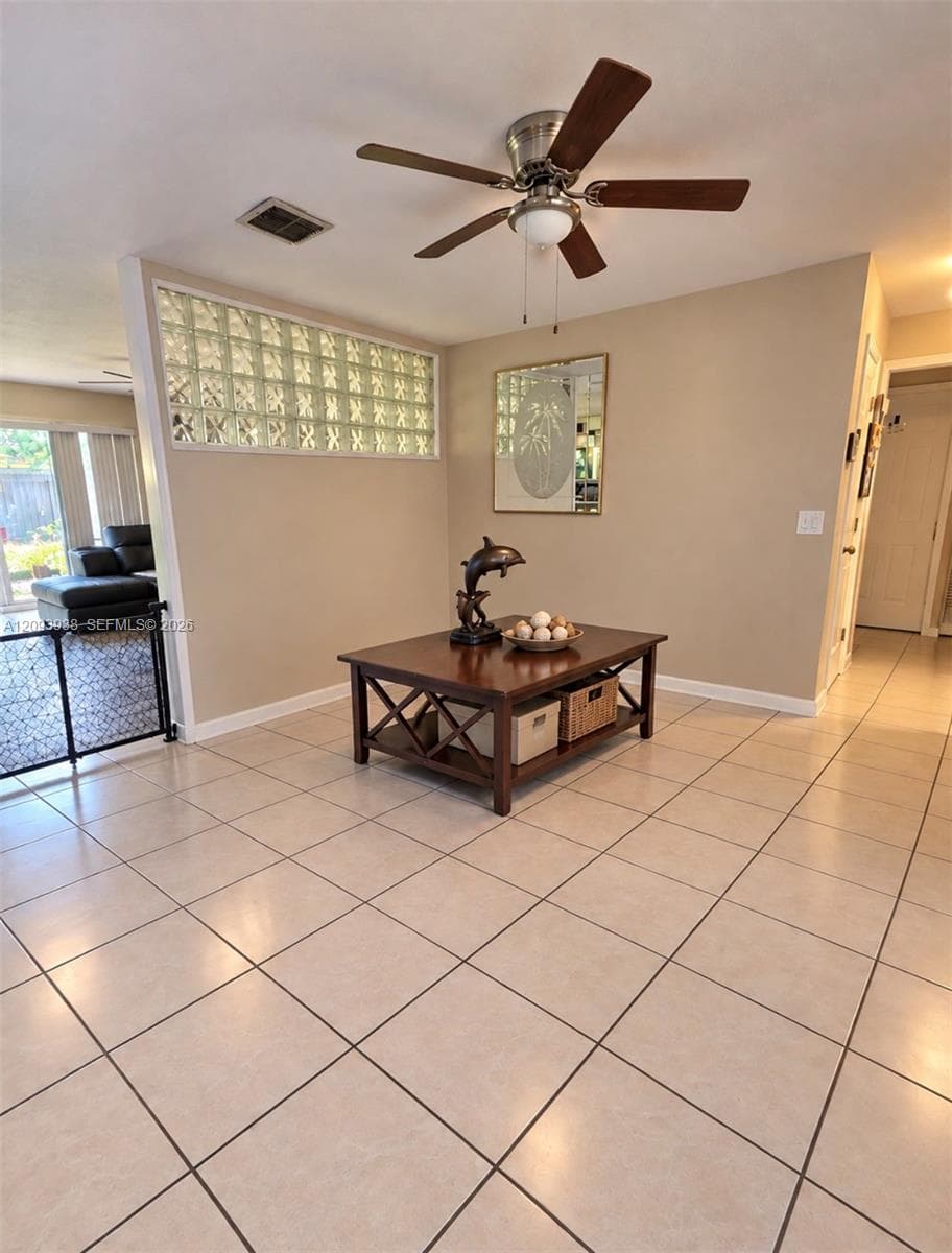 Neutral tile flooring, glass block accent wall, and a central ceiling fan with integrated lighting