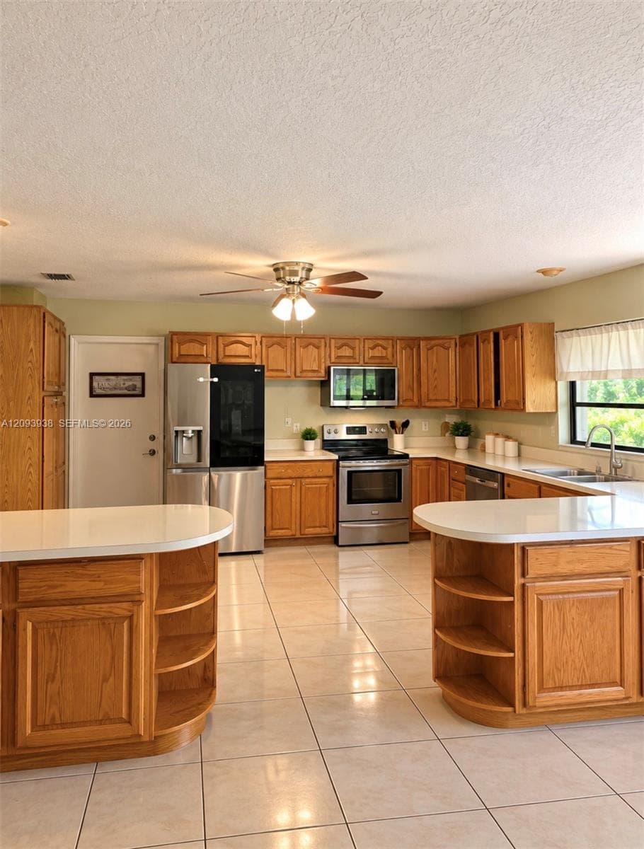 Kitchen featuring warm-toned wood cabinetry, stone countertops, stainless steel appliances, ceramic tile flooring, and dual built-in curved end-cap shelving units