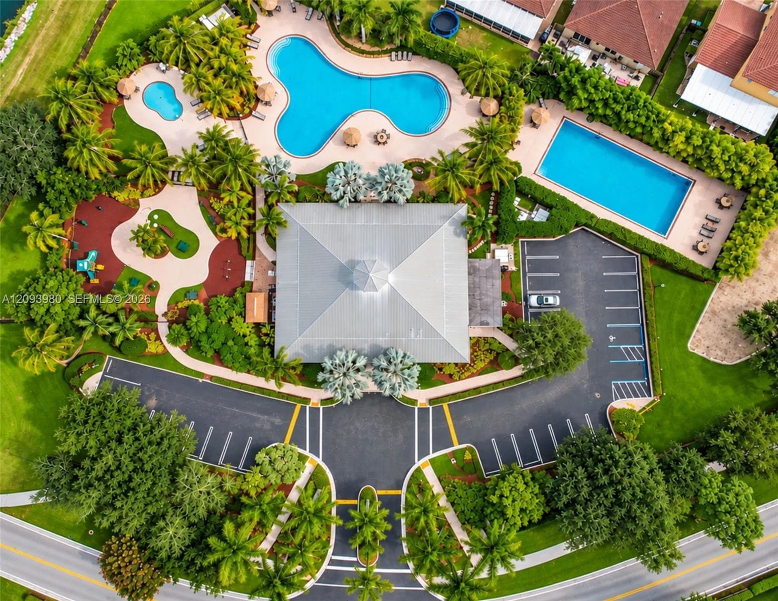 Community amenities featuring multiple swimming pools, a central clubhouse with a metal roof, dedicated parking areas, and landscaped grounds with paved walking paths