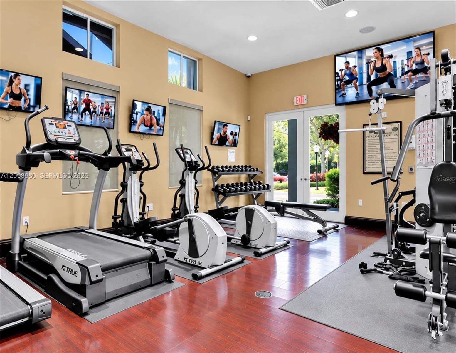 Fitness center featuring wood-finish flooring, recessed lighting, double glass-panel entry doors, and multiple wall-mounted televisions