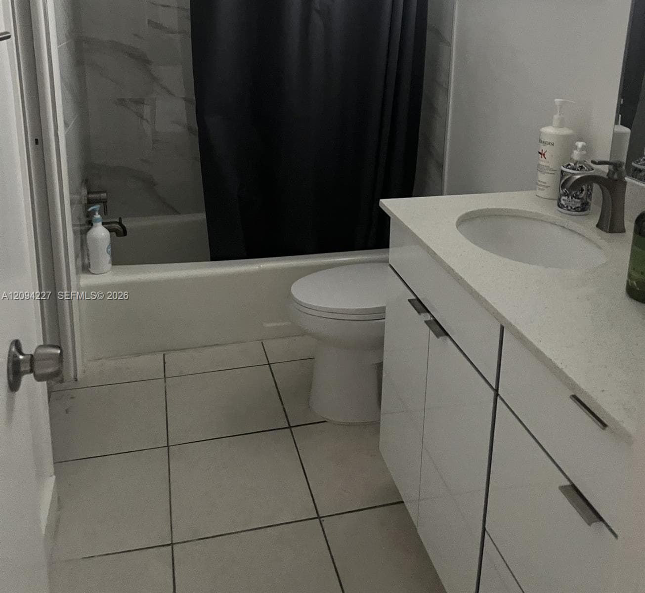 White vanity featuring a composite countertop with an integrated basin, brushed-metal hardware, tile flooring, and a tub-shower combination with surround tile