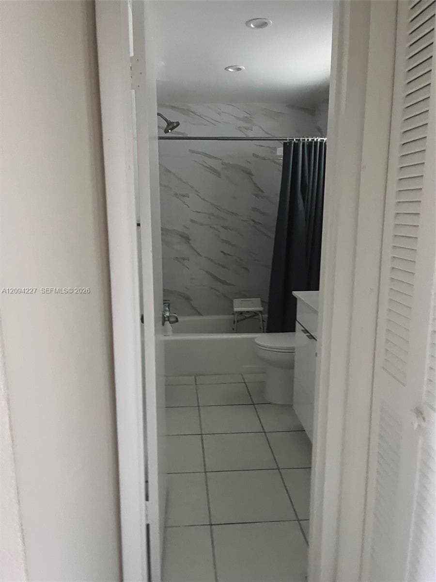 Bathroom featuring large-format floor tiling, a white vanity cabinet, recessed ceiling lighting, and a bathtub surround with full-height decorative wall tile