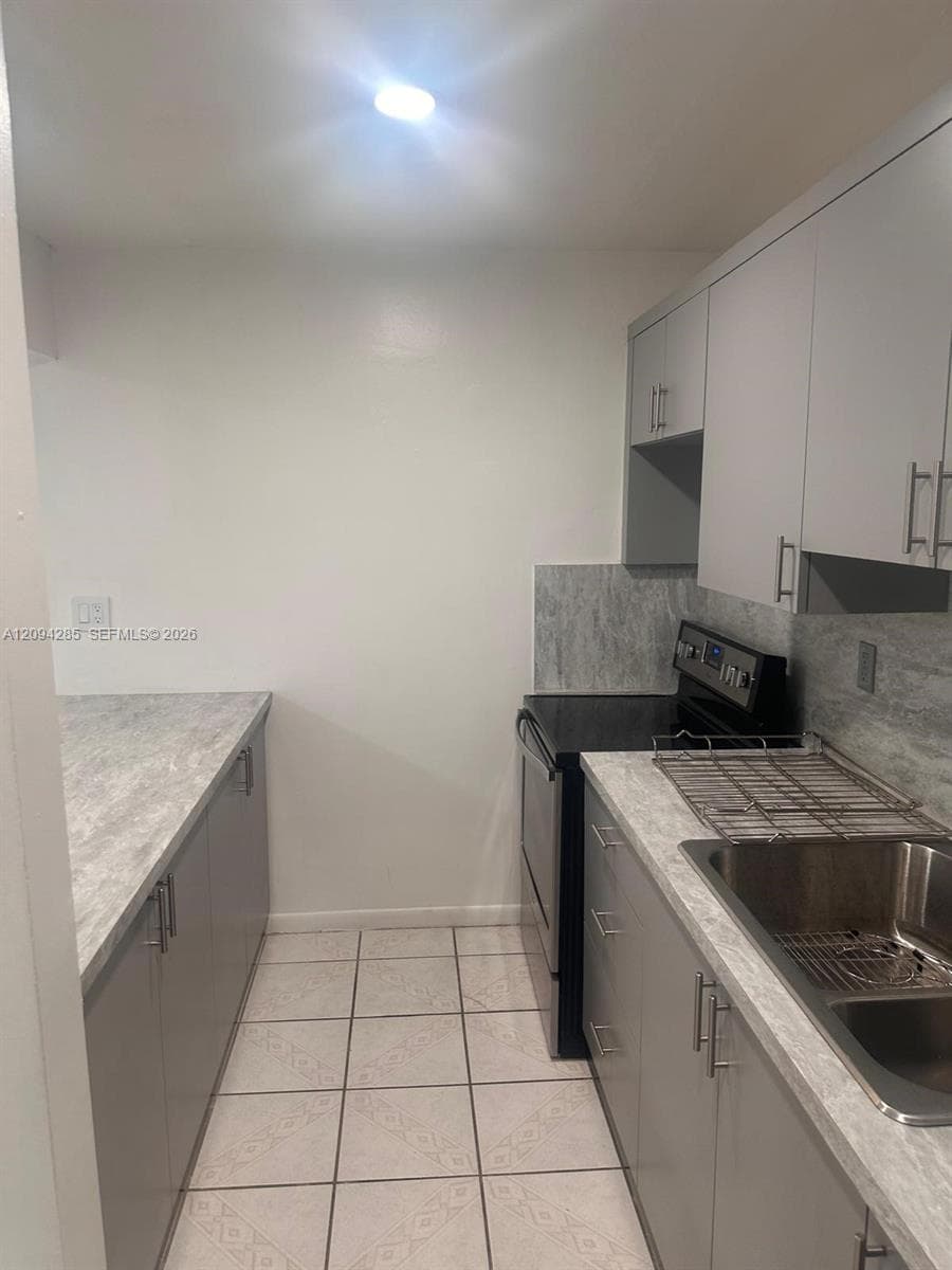 Kitchen featuring flat-panel gray cabinetry, stone-patterned countertops, a stainless steel dual-basin sink, and tile flooring